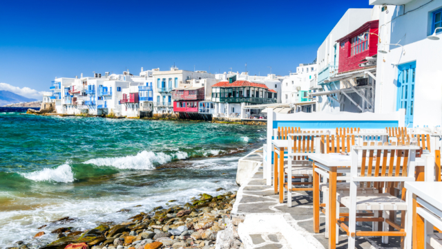 Photo: Adobe Stock. Chairs and tables at the sea front with white and coloured houses